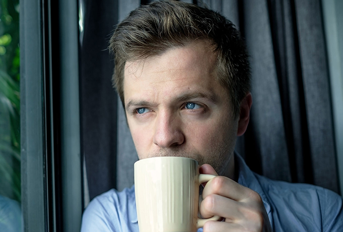 Man staring out window drinking coffee