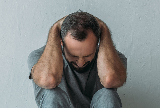 Man sat with head in hands thinking about self-harm