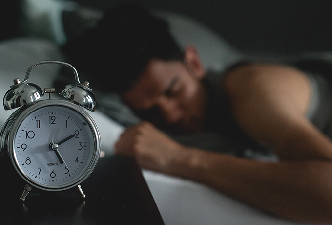 Benefits of sleep header: Man sleeping next to an alarm clock